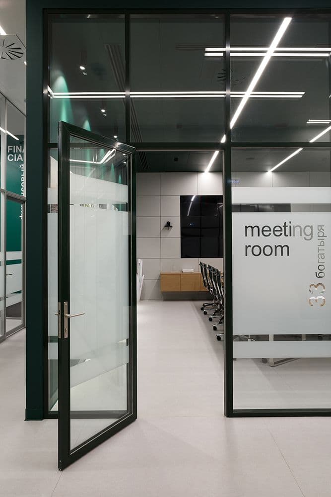 Open glass door to a modern meeting room with minimalist furniture and bright linear lighting.
