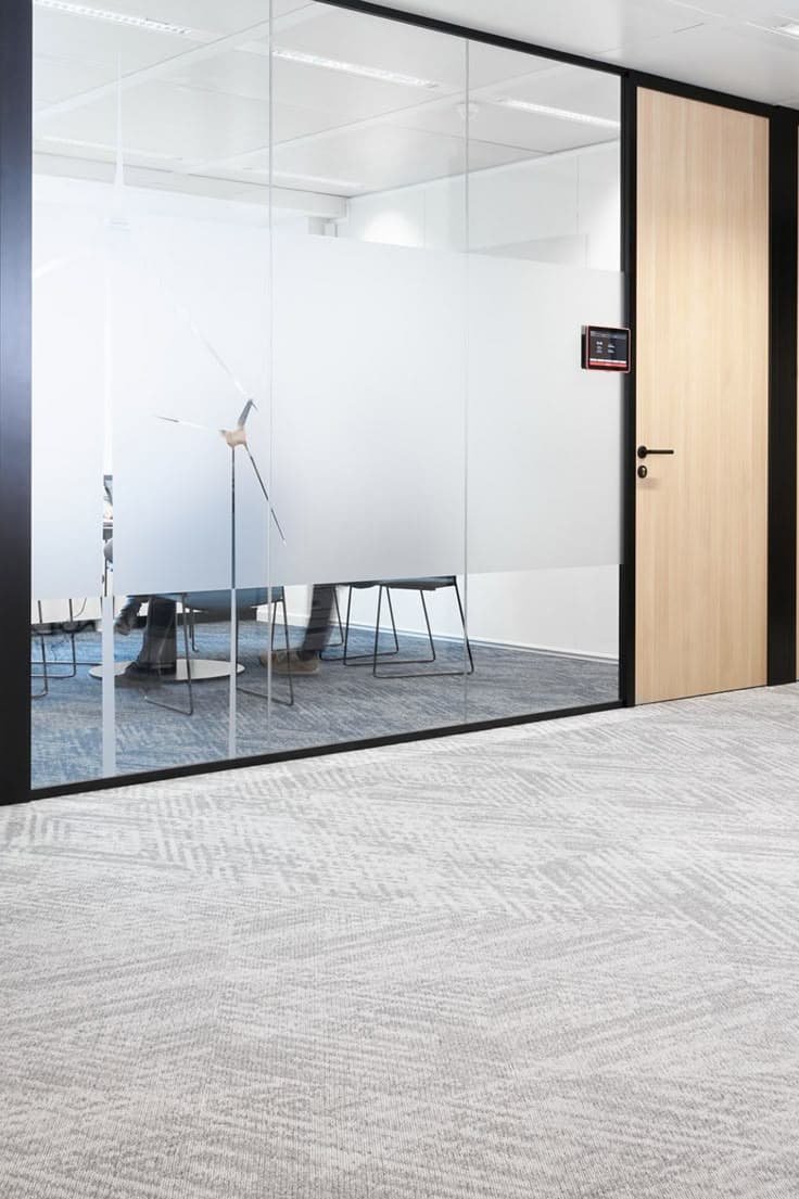 Glass-walled office meeting room with frosted privacy film, wooden door, and grey patterned carpet.