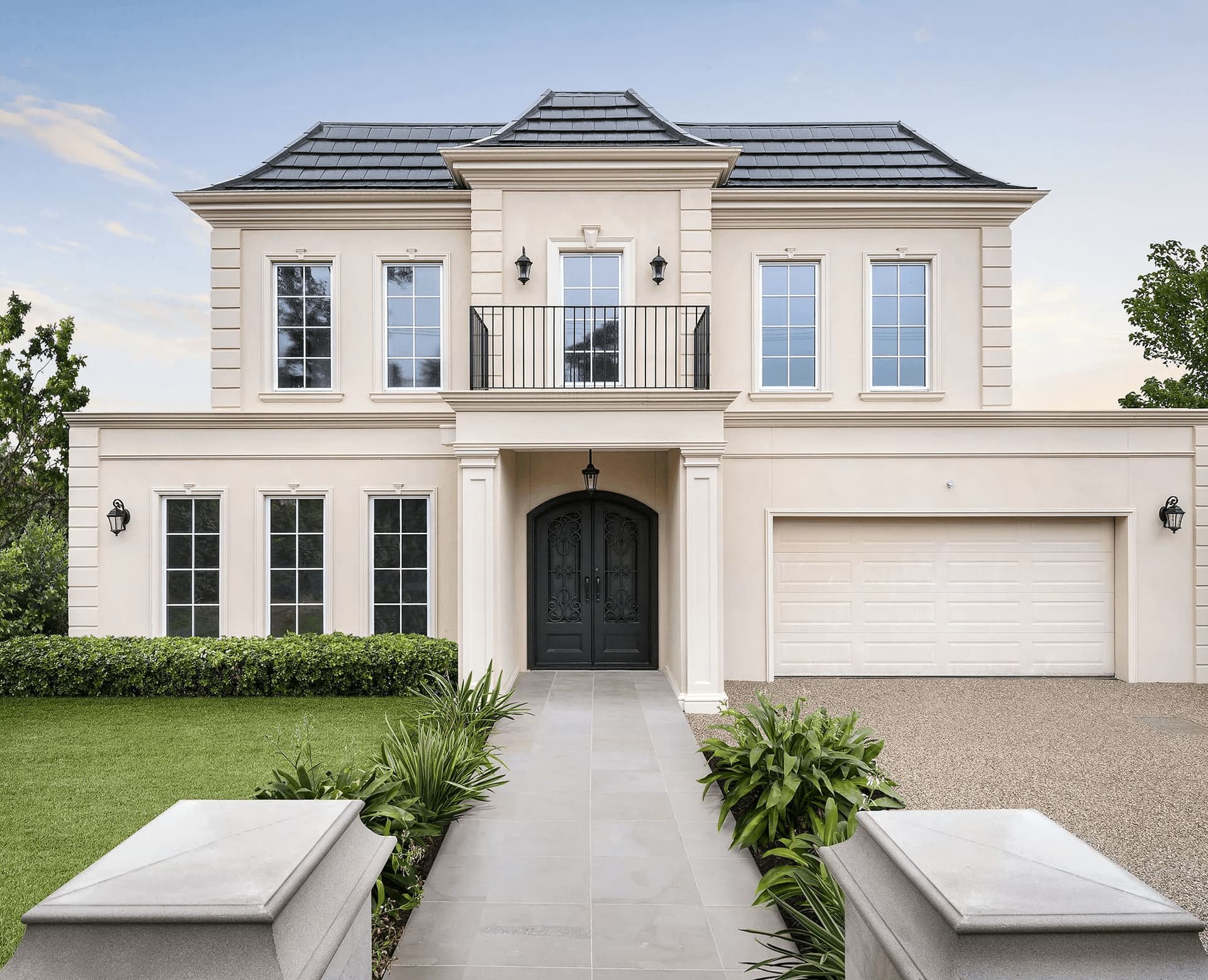 Symmetrical two-story beige home with a black tiled roof, arched door, and stone walkway.